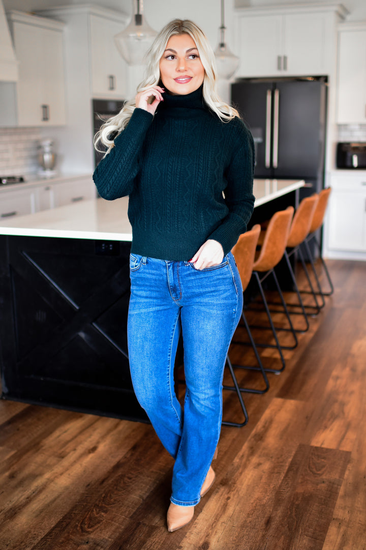 Woman in teal sweater and blue jeans standing in a modern kitchen.