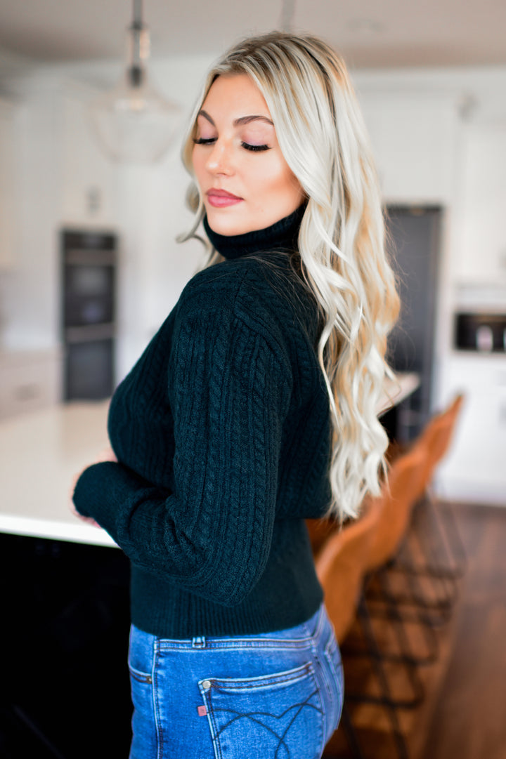 Woman wearing a dark green sweater and blue jeans in a kitchen setting