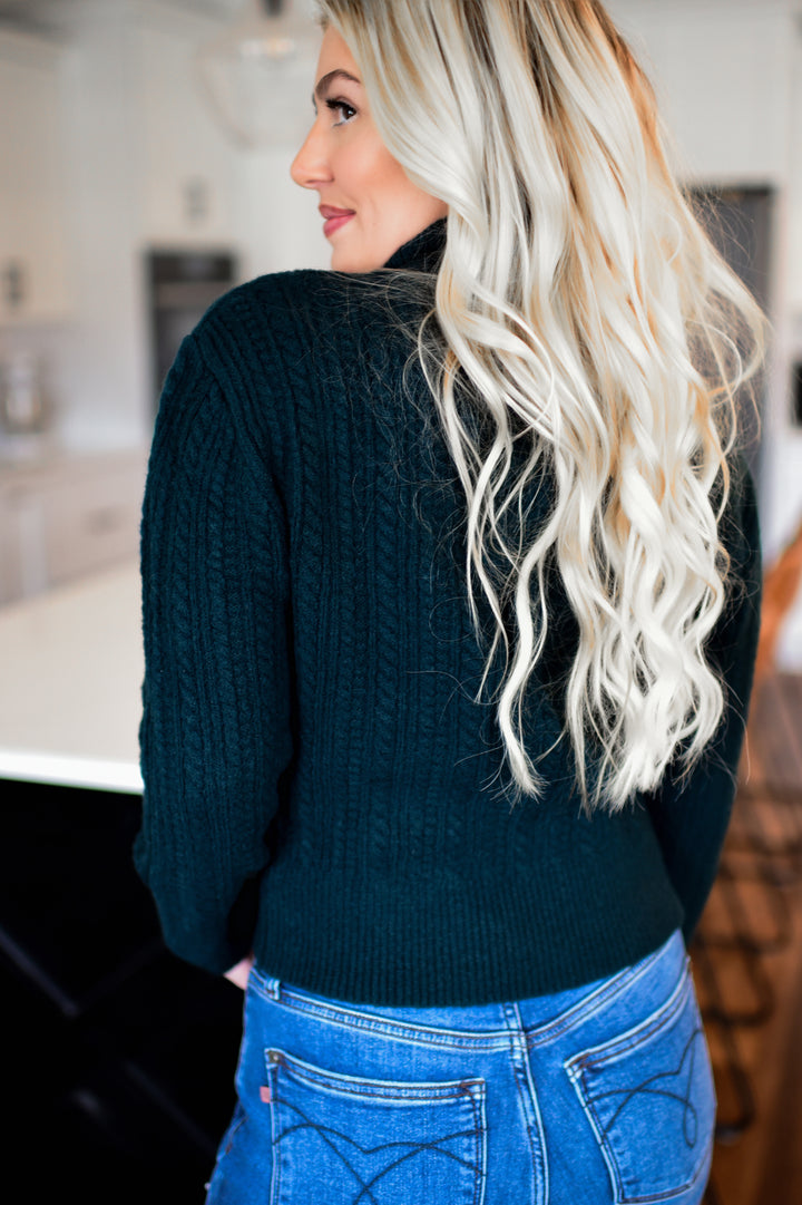 Woman wearing a dark green sweater and blue jeans in a kitchen setting